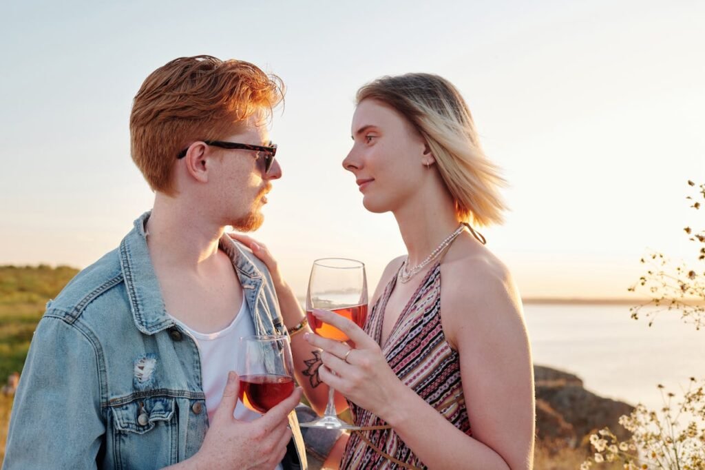 A couple enjoying a romantic evening with rose wine by the water at sunset.