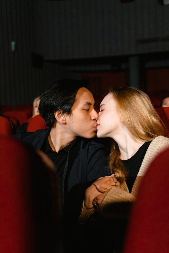 A couple shares a tender kiss while holding hands in a movie theater.