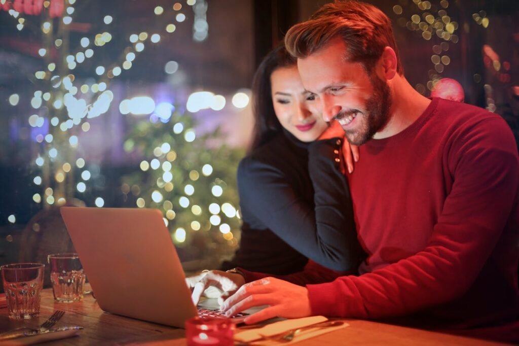 A couple using a laptop at a cozy restaurant with festive bokeh lights, enjoying online shopping together.